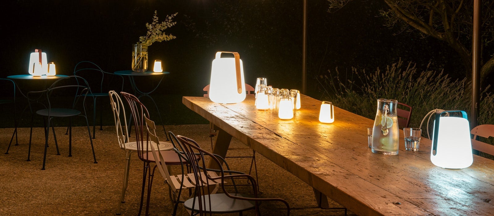 Fermob Balad Akkuleuchten in Acapulcoblau auf einer abendlichen Terrasse mit Hoop Sesseln